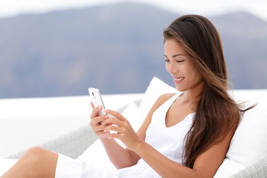 Happy young woman using smartphone while relaxing on couch. Beautiful female is at resort terrace. Happy tourist is spending leisure time during vacation.