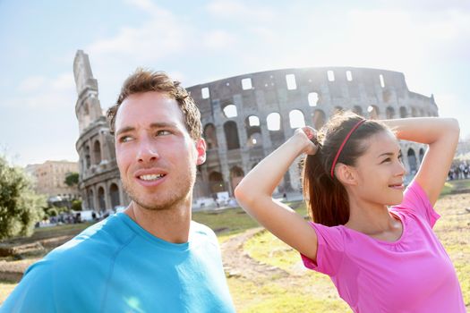 People Running  by Colosseum in Rome. Jogging couple going for run. Woman and man runners are in sportswear. Woman is tying ponytail while preparing for workout on sunny day.