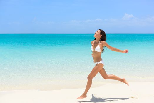 Beach bikini woman carefree running in freedom fun. Joyful happy Asian girl relaxing showing joy and happiness in slim body for weight loss diet concept on perfect white sand.