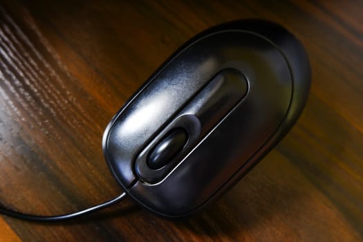 top view of black color computer mouse isolated on brown wooden texture