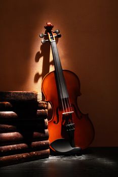 Nice violin near stack of old books against yellow wall