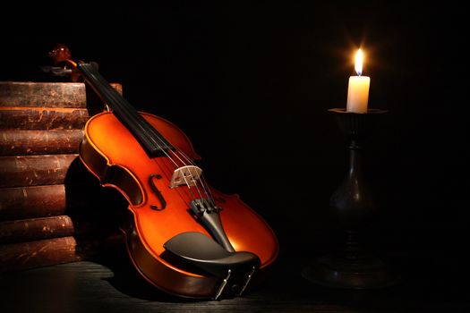 Nice violin near stack of old books and candle against black background