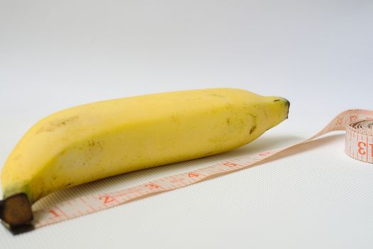 Penis size concept using ripe banana and soft measuring tape in white background