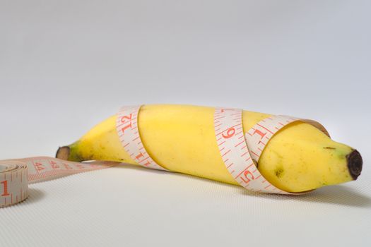 Penis size concept using ripe banana and soft measuring tape in white background