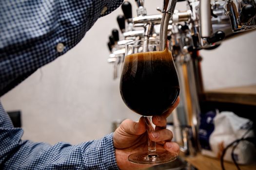 The bartender pours fresh black beer from tap in the pub