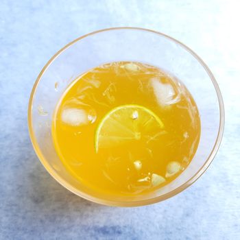 Lemon juice in glass with added orange syrup and ice cubes and slice of lemon inside placed beautifully in white background