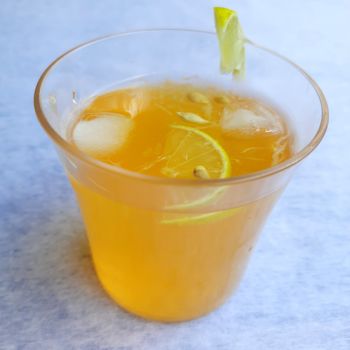 Lemon juice in glass with added orange syrup and ice cubes and slice of lemon inside and outside of glass placed beautifully in white background