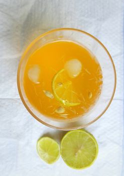 Lemon juice in glass with added orange syrup and ice cubes and half slice of lemon inside and outside of glass placed beautifully in white background