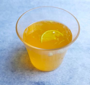 Lemon juice in glass with added orange syrup and slice of lemon inside placed beautifully in white background