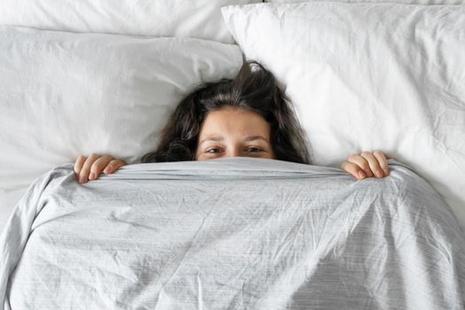 The girl does not want to get out of bed in the morning. Hiding in a blanket. View from above. Ambush in bed.