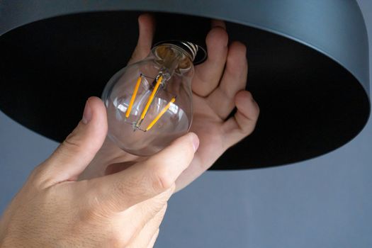 Close-up. A hand changes a light bulb in a stylish loft lamp. Spiral filament lamp. Modern interior decor