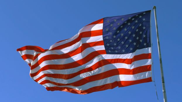 USA flag on flagpole. American flag - symbol of freedom and law in the USA. American flag flies in the sky as a symbol of the Great Country of the USA. Big American flag against blue sky.