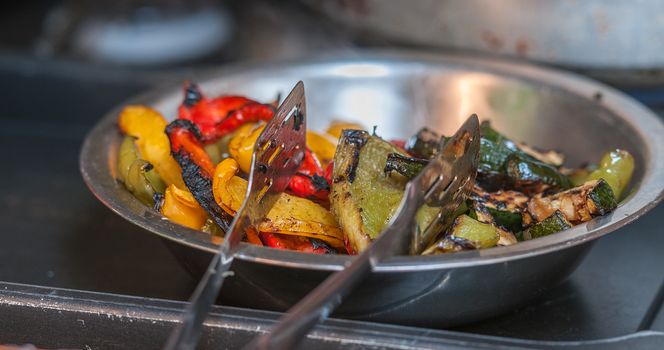 mixed cooked peppers in a dish with thongs