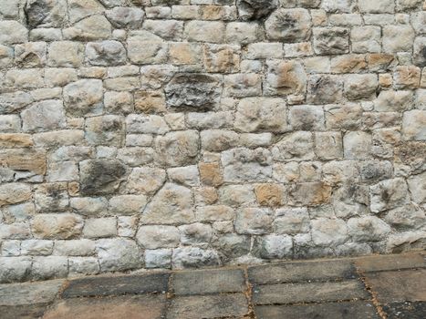 Ancient stone wall paved with cobblestone with stone pavement at an angle. Stone wall building feature. Background image of weathered stained old stone wall of rough stones of various shapes and sizes