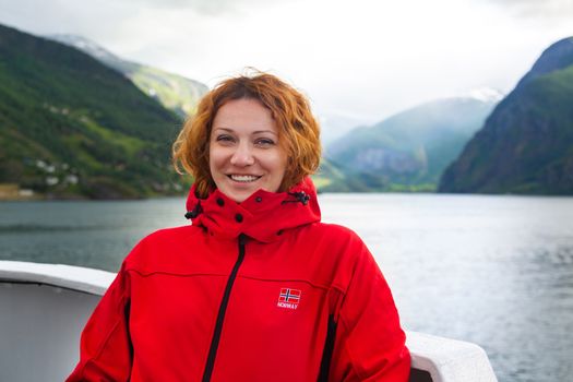 Young beautiful woman in smiling against the background of a Norwegian fjord. Woman on the deck of a ship in Norway. Journey through the Norwegian fjords. Tourist concept. Journey on the ferry boat.