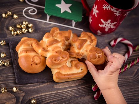 Christmas background with ruddy gingerbread and homemade cookies. Children's hand reaches for cookies. Close-up, top view. Background with tasty cookies, cup of coffee and Christmas decor wooden table