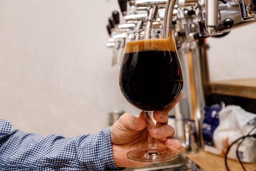 The bartender pours fresh dark beer from tap in the pub