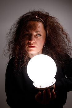 Fortuneteller holding a glowing ball in her hands. Alertness on face