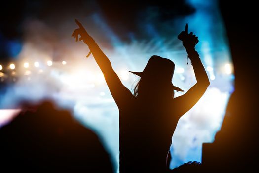 Silhouette of girl with raised hands on music concert.