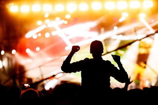 A man silhouette with his hands up at a concert of his favorite group. Light from the stage