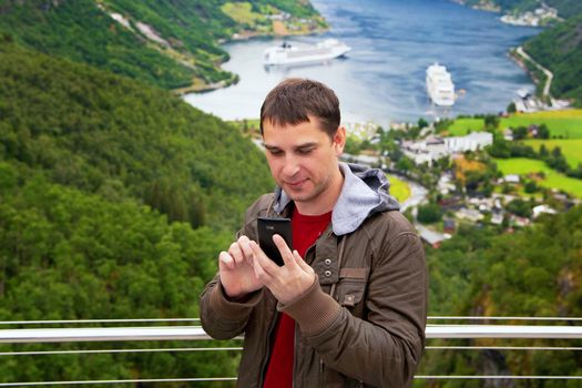 Men poses on camera and does selfi near Geiranger, Norway. End of the famous Geiranger fjord, Norway with cruise ship, top view. Geiranger View Point. Tourism holidays and travel.