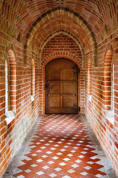 Wooden ancient door at the end of the brick corridor with arches.