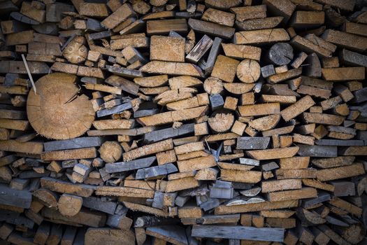 Firewood background - stacked chopped wooden logs backdrop. Background of firewood stack. Pile of chopped fire wood, background. Composition of the cut firewood. Vignette around the perimeter.