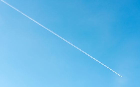Diagonal contrail of jet plane flying in blue sky