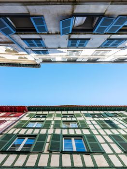 Looking up at old building facades in Bayonne, France. Windows with colorful shutters, half-timbered house at the bottom and blue sky in the middle.