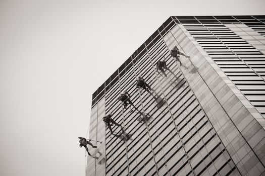 Laborers clean windows as a team on a skyscraper in downtown Singapore