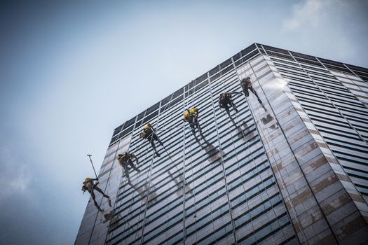 Laborers clean windows as a team on a skyscraper in downtown Singapore