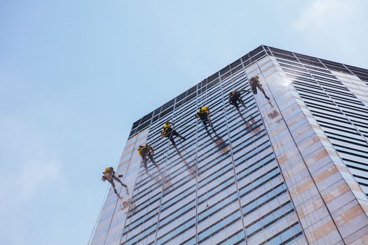 Laborers clean windows as a team on a skyscraper in downtown Singapore