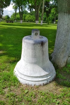 Old white bell on the grass in the church park. Ukrainian monument