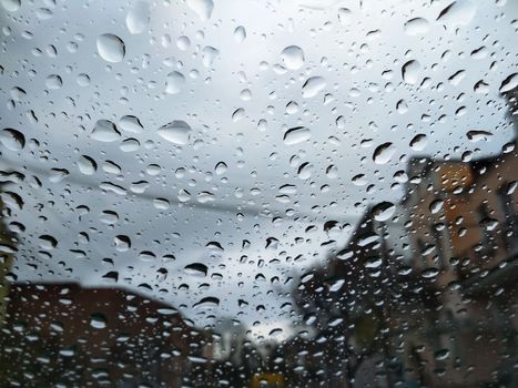 City street seen through rain drops on the car windshield. Focus is on some water drops. Bad Autumn weather in Rainy day. Windshield window of car with raindrops on glass windscreen.