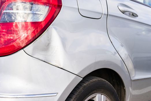 Car crash with detail view of damaged dented and scratched silver bumper and fender