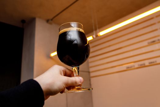 Black beer glass in hands. Pub interior