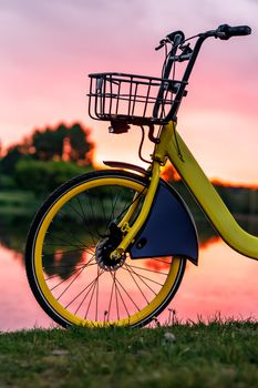 Front wheel of a yellow bike on the lake. Sunset pink sky