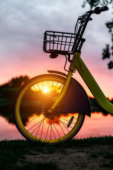 Front wheel of a yellow bike on the lake. Sunset pink sky