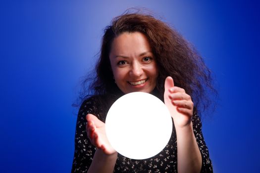Smiling girl holding a glowing ball in her hands. Blue background
