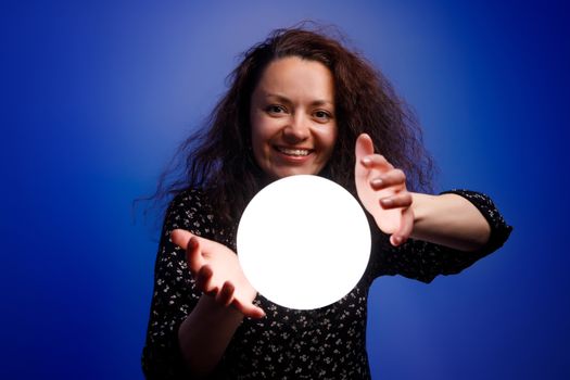 Smiling girl holding a glowing ball in her hands. Blue background