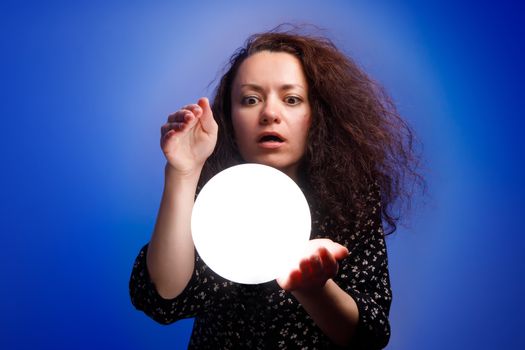 Smiling girl holding a glowing ball in her hands. Blue background