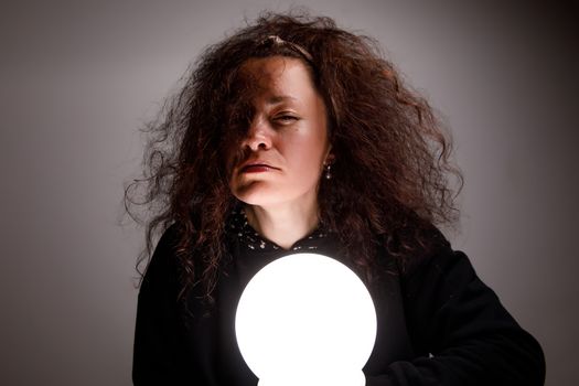 Fortuneteller holding a glowing ball in her hands. Alertness on face