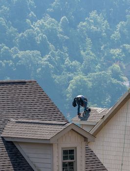 Young roofing contractor replacing the old shingles on a townhouse roof high above the ground