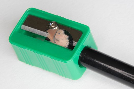 Green pencil sharpener with a black pencil on a white background