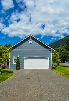 Garage door of residential house on a country side with asphalt road in front. Garage door and driveway of family home in British Columbia, Canada