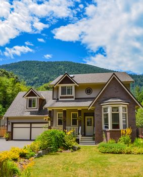 Big family house with wide garage and decorated front yard with mounting and blue sky background