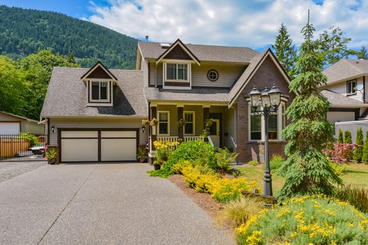 Big family house with wide concrete driveway, double garage door, decorated front yard. Residential house with mounting and blue sky background