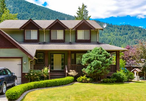 Big family house with hedge and  draw-well decorating the front yard on mounting and blue sky background