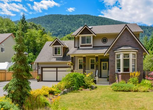 Big family house with wide garage and decorated front yard on mounting and blue sky background