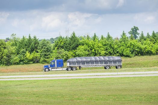 Horizontal shot of a blue 18-wheeler with a covered bed traveling down a Tennessee highway.